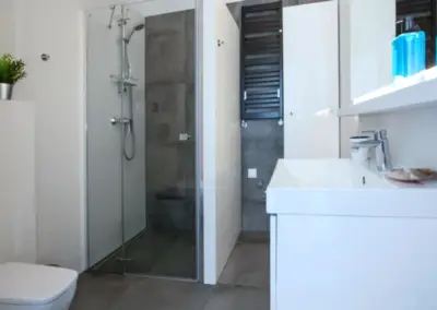 Modernes Badezimmer im Ferienappartement Dziwnów mit Dusche, Waschbecken, WC und hellen Fliesen.