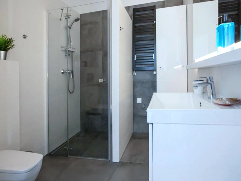 Modernes Badezimmer im Ferienappartement Dziwnów mit Dusche, Waschbecken, WC und hellen Fliesen.