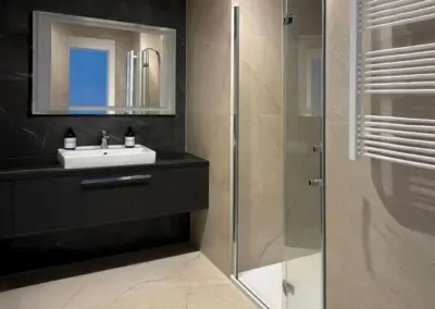 Modernes Badezimmer im Ferienappartement in Misdroy mit Waschtisch, Spiegel, bodengleicher Glasdusche und Handtuchheizkörper.