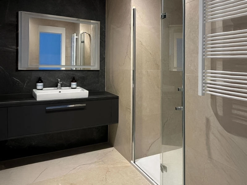Modernes Badezimmer im Ferienappartement in Misdroy mit Waschtisch, Spiegel, bodengleicher Glasdusche und Handtuchheizkörper.
