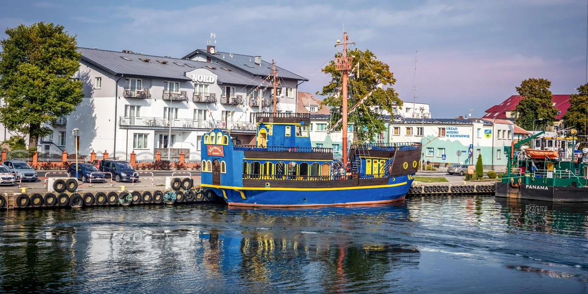 Historisches, restauriertes Schiff im Hafen von Dziwnów (Polen) an der Hafenmole und Gebäuden an der Promenade.