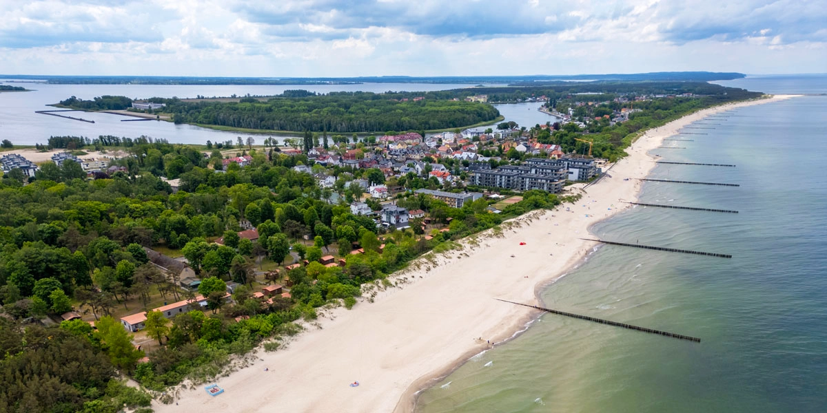 Luftaufnahme von Dziwnów an der polnischen Ostsee mit Sandstrand, Küstenbebauung, Flusslauf und grüner Umgebung.