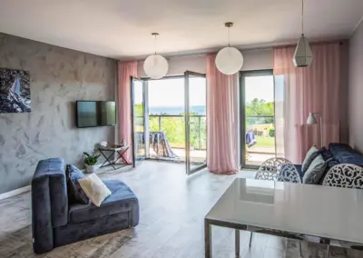 Heller Wohnbereich im Ferienappartement Dziwnów mit Schlafcouch, Essplatz und Balkonzugang mit Blick ins Grüne.