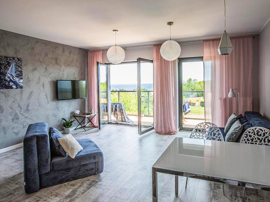 Heller Wohnbereich im Ferienappartement Dziwnów mit Schlafcouch, Essplatz und Balkonzugang mit Blick ins Grüne.