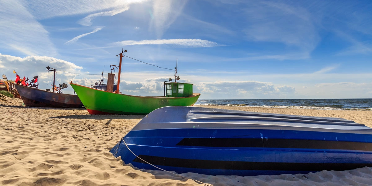 Fischerboote am Sandstrand von Misdroy mit blauem Boot im Vordergrund, Ostsee und blauem Himmel.