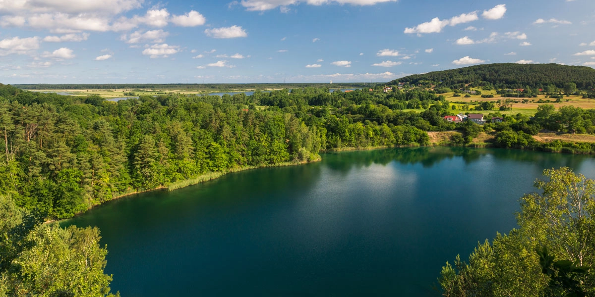 Blick über den Nationalpark Wollin mit tiefblauem See, dichten Wäldern und weiter Landschaft unter blauem Himmel.