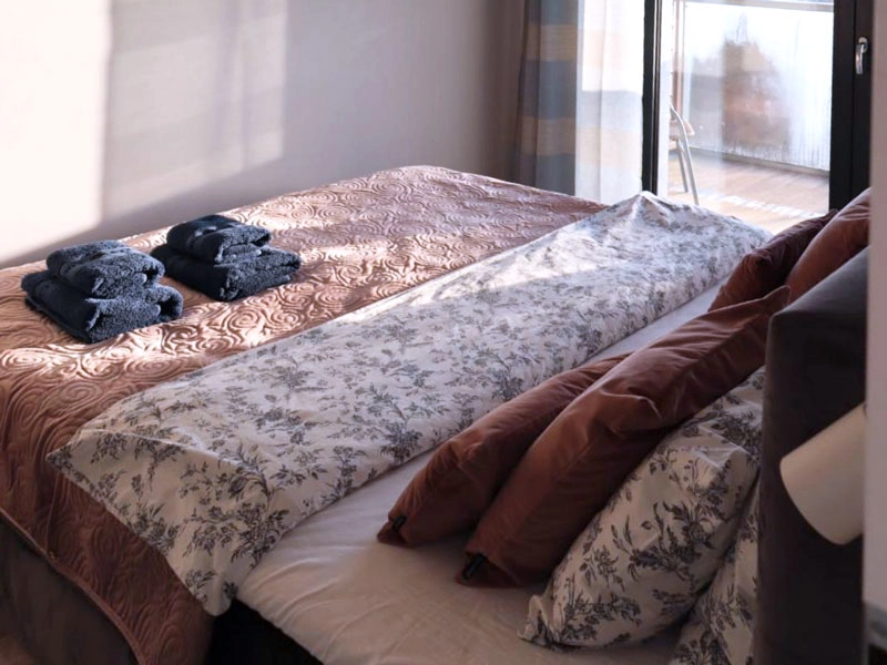 Gemütliches Schlafzimmer im Ferienappartement Dziwnów mit Doppelbett, Tageslicht und Zugang zum Balkon.