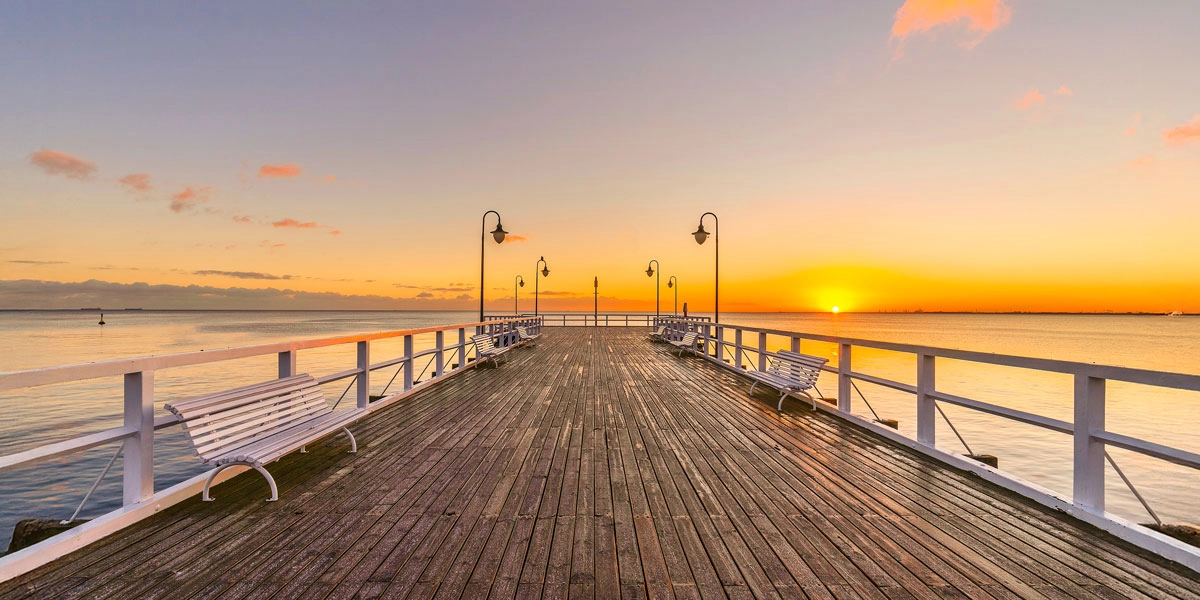 Seebrücke in Misdroy (Polen) bei Sonnenuntergang mit Holzdielen, Bänken und Laternen über ruhiger Ostsee.