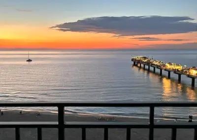 Blick vom Balkon auf die beleuchtete Seebrücke von Misdroy bei Sonnenuntergang über der ruhigen Ostsee.