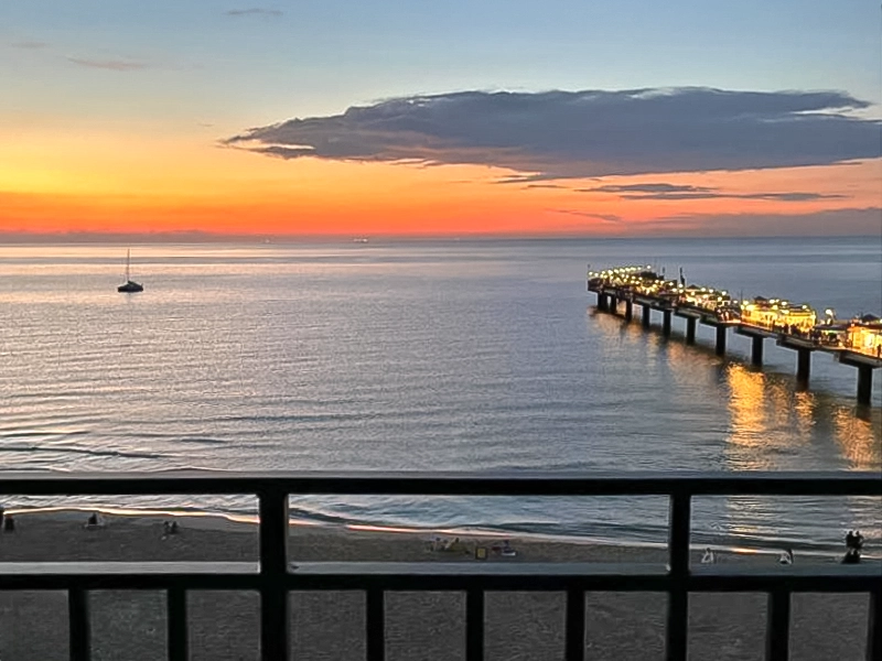 Blick vom Balkon auf die beleuchtete Seebrücke von Misdroy bei Sonnenuntergang über der ruhigen Ostsee.