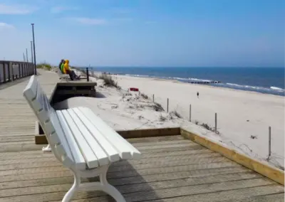 Strandpromenade in Dziwnów mit Sitzbank, Holzsteg und Blick auf den Sandstrand und die Ostsee.