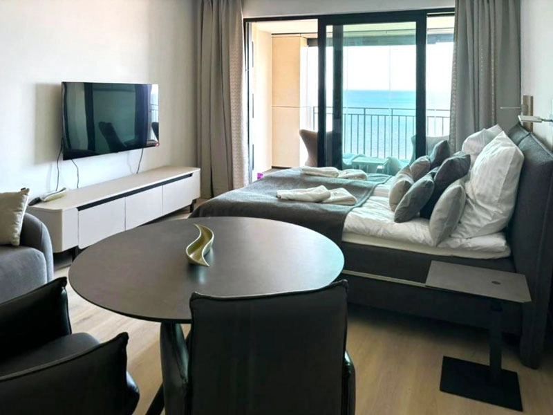 Wohnzimmerbereich im Ferienappartement in mit Schlafcouch (ausziehbar zum Bett), Esstisch, TV und Balkon mit Meerblick.