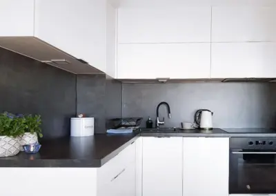 Moderne Küchenzeile im Ferienappartement Dziwnów mit weißen Schränken, dunkler Arbeitsfläche und Einbaugeräten.