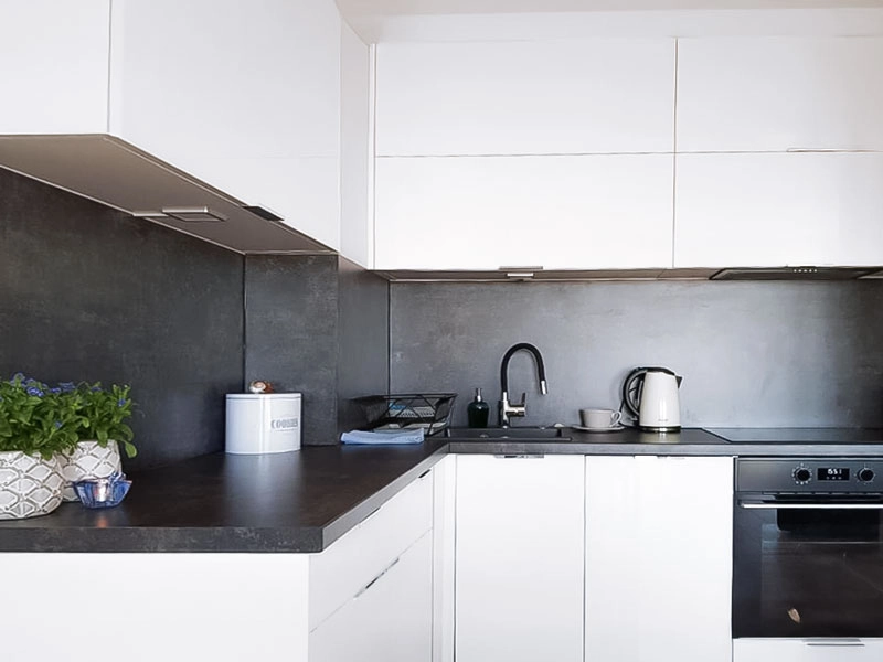 Moderne Küchenzeile im Ferienappartement Dziwnów mit weißen Schränken, dunkler Arbeitsfläche und Einbaugeräten.